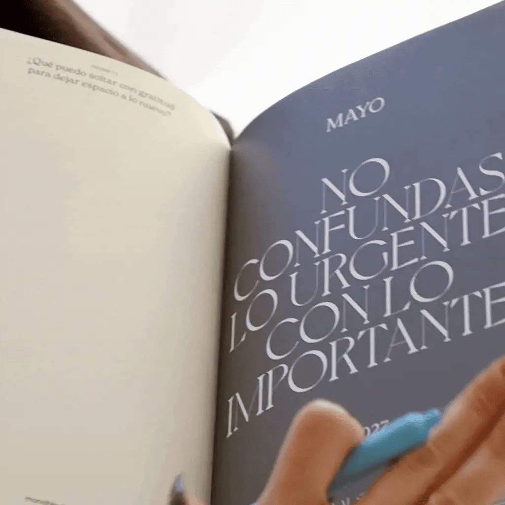 Interior de la Agenda 2027 negra Journal Sessions abierta en mayo con página de frase inspiradora No confundas lo urgente con lo importante en tipografía grande sobre fondo azul grisáceo

