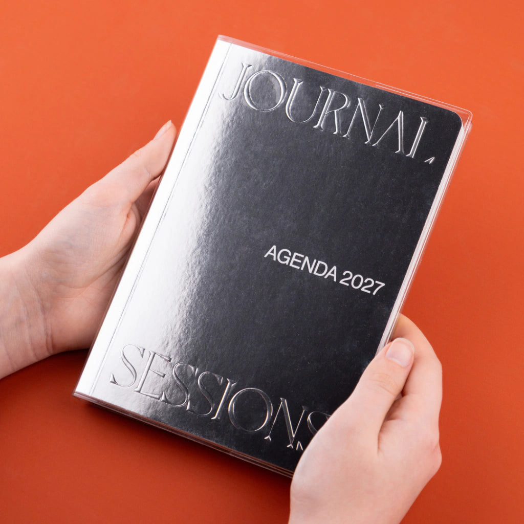 Detalle de la cubierta protectora transparente de la Agenda 2027 negra Journal Sessions con texto JOURNAL SESSIONS en relieve plateado y la palabra AGENDA 2027 visible en la portada
