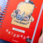 Detalle de la portada de la agenda diaria para 2027 Sillón con organización a día por hoja e ilustración de Liniers de Enriqueta leyendo en un sillón rodeada de otros personajes de Macanudo
