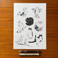 Ilustración de gatos de Laura Agustí en print A4 sobre una mesa de madera