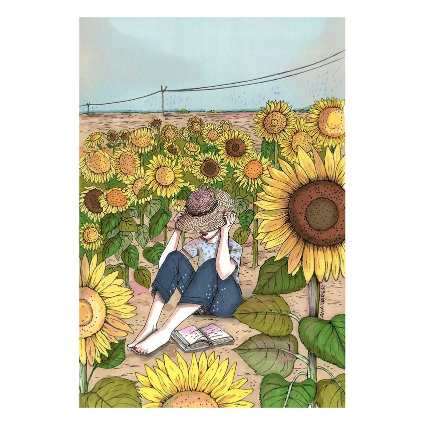 Una mujer se ajusta el sombrero sentada en el suelo en medio de un campo de girasoles gigantes. A sus pies, descalzos, reposa un libro abierto.