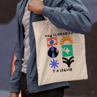 foto de un modelo llevando la tote bag de wo! blnca con el texto una lloradita y a seguir. Con dibujos abstractos de colores