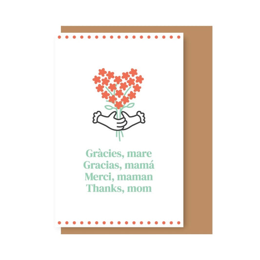 Tarjeta ilustrada con flores rojas en forma de corazón sujetadas por unas manos. Debajo se lee "Gràcies, mare. Gracias, mamá. Merci, maman. Thanks, mom" en diferentes idiomas, sobre fondo blanco con una cenefa de puntos rojos arriba y abajo. Detrás, un sobre de color kraft. 