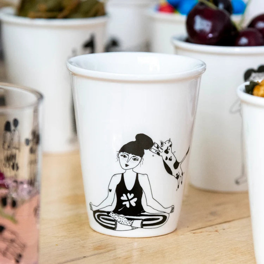 Taza en blanco y negro de una mujer meditando mientras un gato le araña la cabeza. 