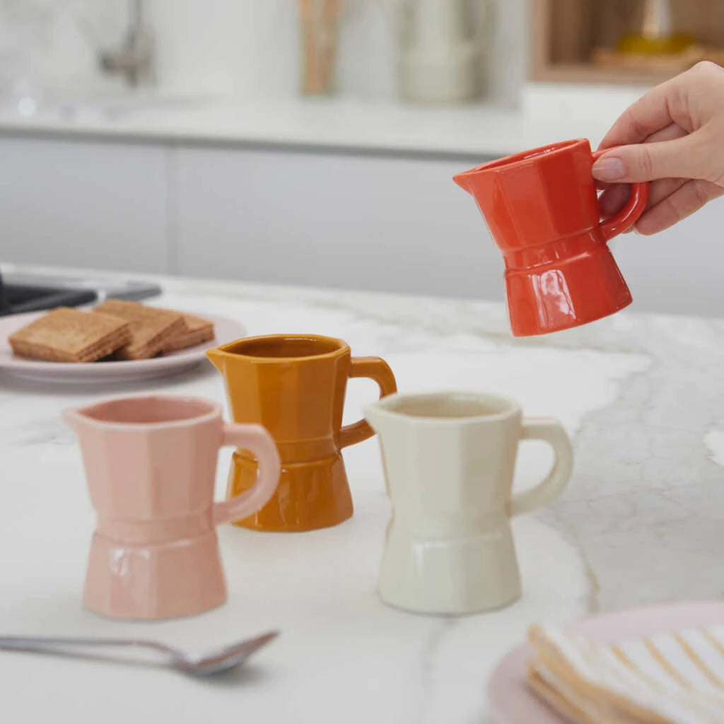 Juego de cuatro tazas de cerámica con forma de cafetera italiana para café cortado en colores pastel: naranja, crema, rosa y mostaza en una sobremesa