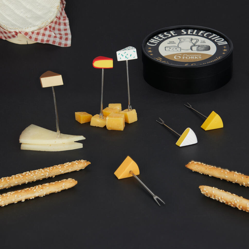Seis tenedores de aperitivo Cheese Selection sobre fondo negro junto a la lata, palitos de pan con sésamo y distintas variedades de queso