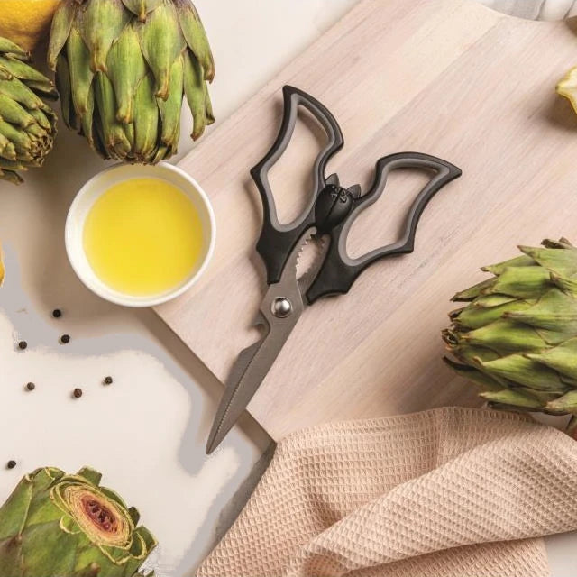 tijeras en forma de murciélago en una tabla de cortar junto a alcachofas y aceite de oliva