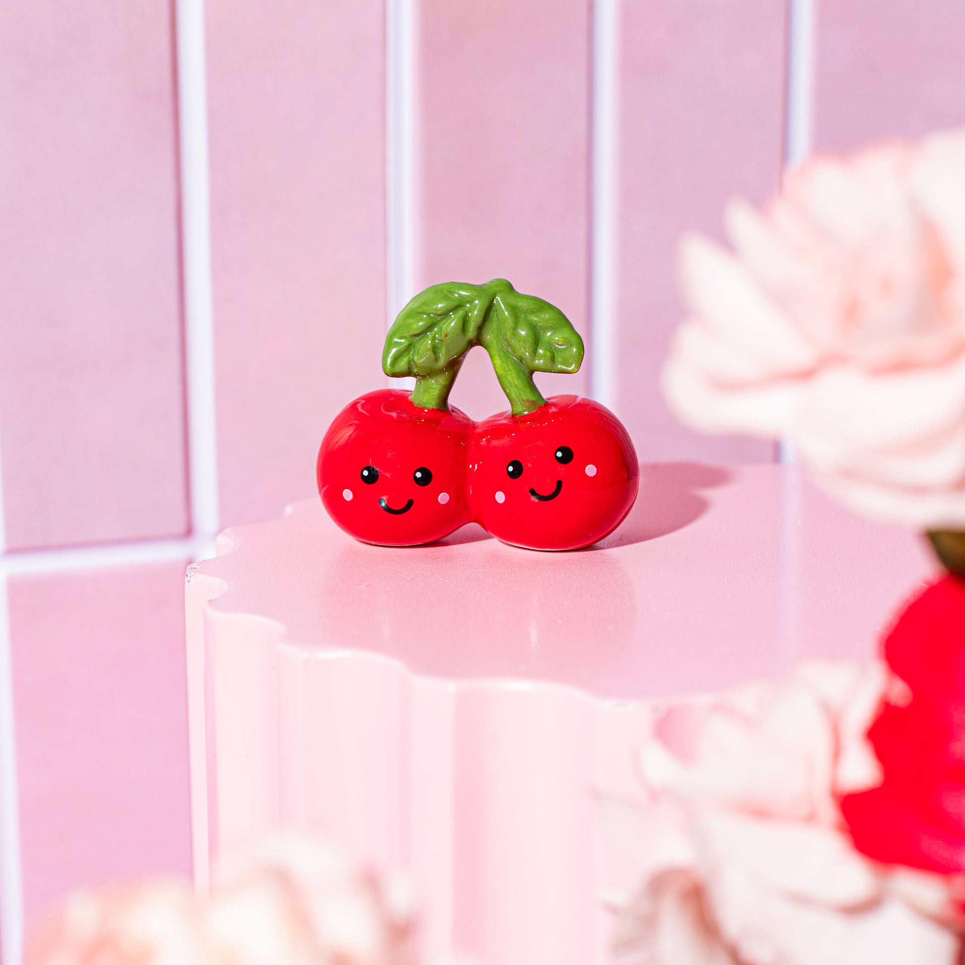 Token de dos cerezas sonrientes sobre fondo rosa y flores. 
