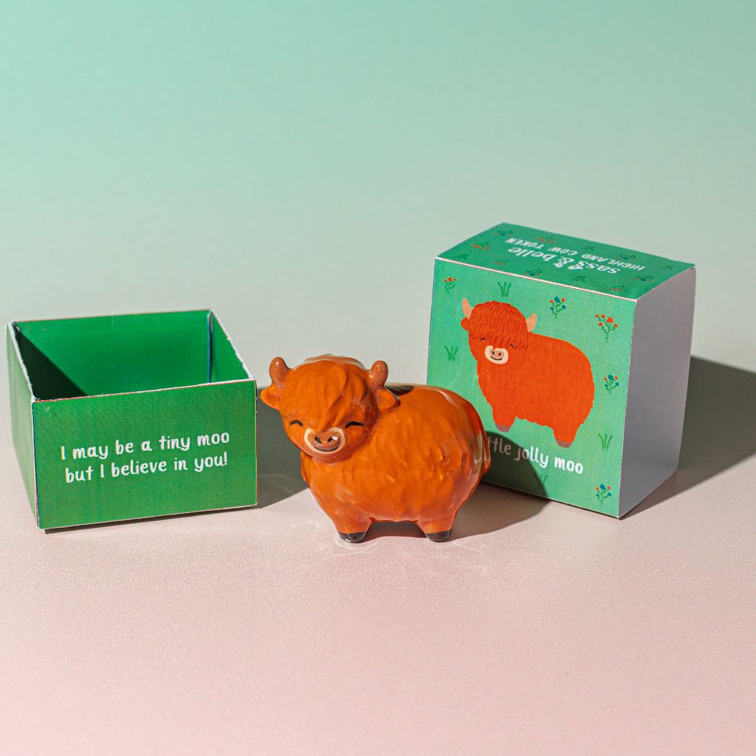 Token de vaca de las tierras altas marrón y sonriente con su respectiva caja en la que pone "I may be a tiny moo but i believe in you!"