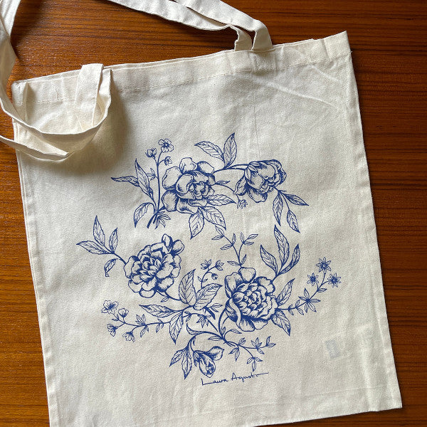 Bolsa de tela o tote bag con ilustración de flores en azul de Laura Agustí sobre una mesa de madera