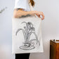 Mujer con una tote bag de tela cruda con ilustración de Laura Agustí de una taza de porcelana de la que sale una planta 