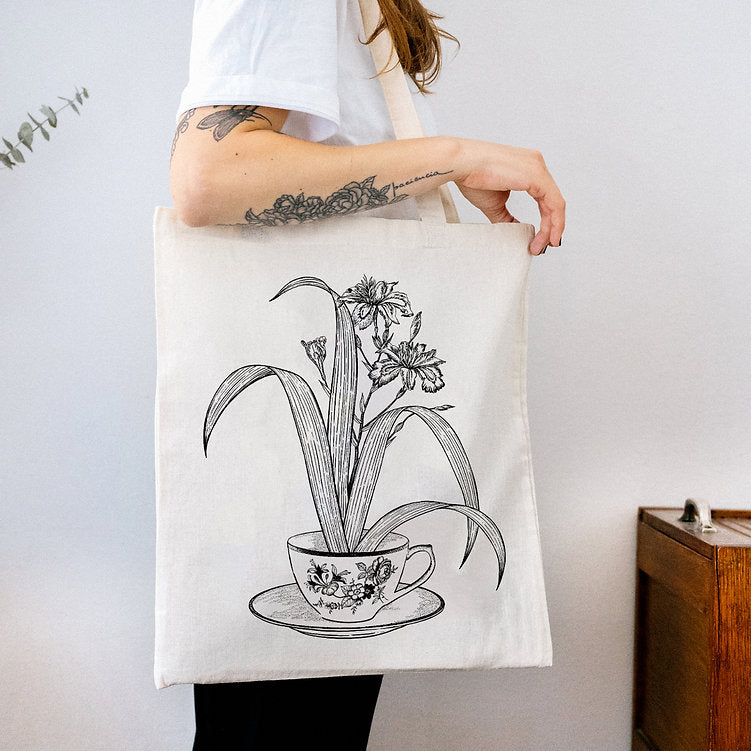 Mujer con una tote bag de tela cruda con ilustración de Laura Agustí de una taza de porcelana de la que sale una planta 