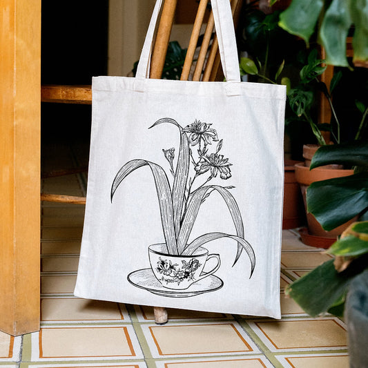 Tote bag de tela cruda con ilustración de Laura Agustí de una taza de porcelana de la que sale una planta colgada en una silla de madera