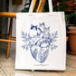 Tote bag de algodón con ilustración de cuatro gatos sobre un corazón anatómico colgada en una silla