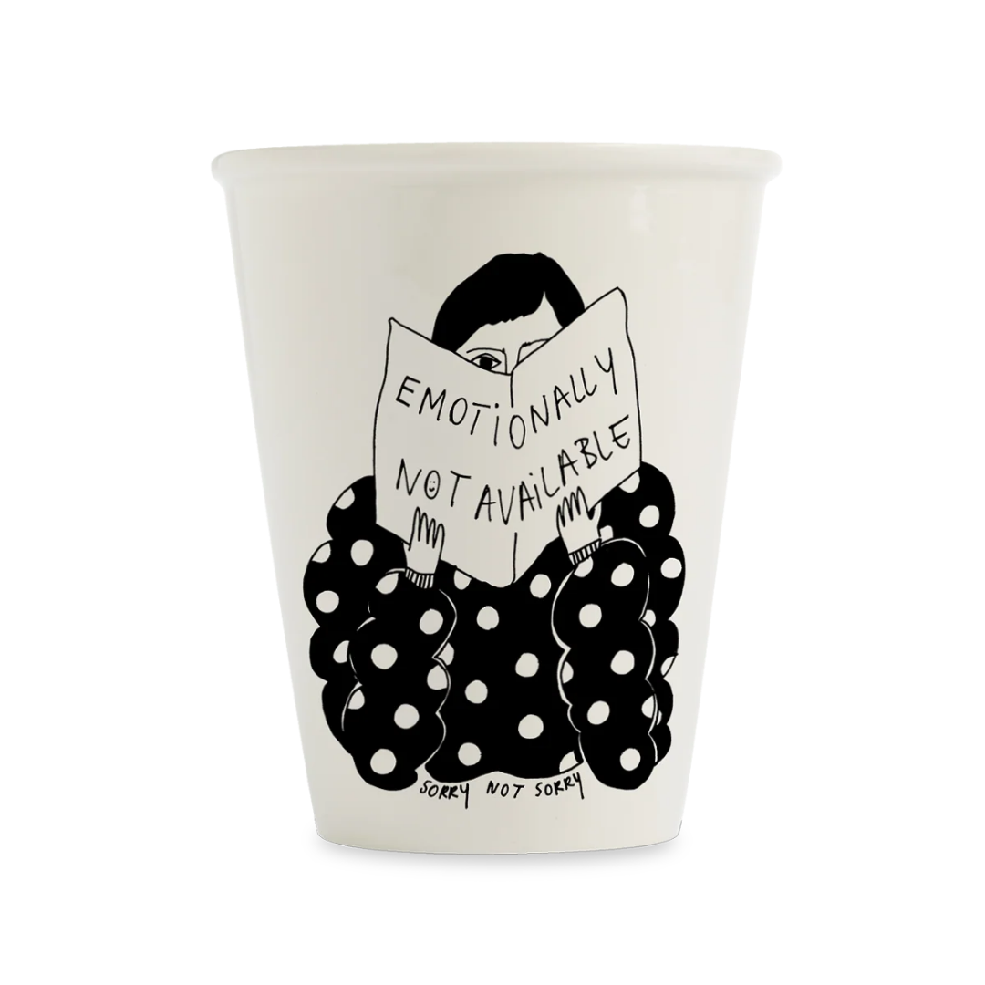 Vaso de porcelana blanca Sorry Not Sorry con ilustración de figura con traje de lunares negros leyendo un libro con texto Emotionally Not Available, vista frontal sobre fondo blanco
