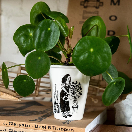 Vaso de cerámica con ilustración de una chica vestida con un mono regando las plantas usado como maceta con una pilea dentro