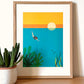 Ilustración de una chica zambulléndose en el mar azul con pececillos, algas y una puesta de sol de fondo en un marco 30x40 color madera 