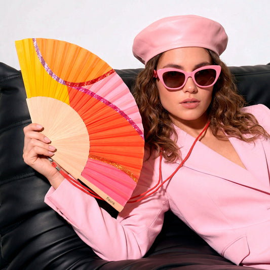 modelo con las gafas de sol better late than ugly y el abanico de la marca fisura con ondas en colores amarillo, naranja y rosa, y con purpurina de colores. 