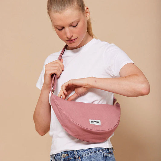 Mujer con camiseta blanca abriendo el bolso riñonera rosa de la marca Hindbag con forma de media luna