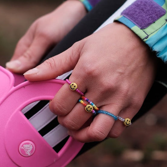 Foto de una mano con anillos de cuentas coloridas y con caritas sonrientes poniéndose las botas