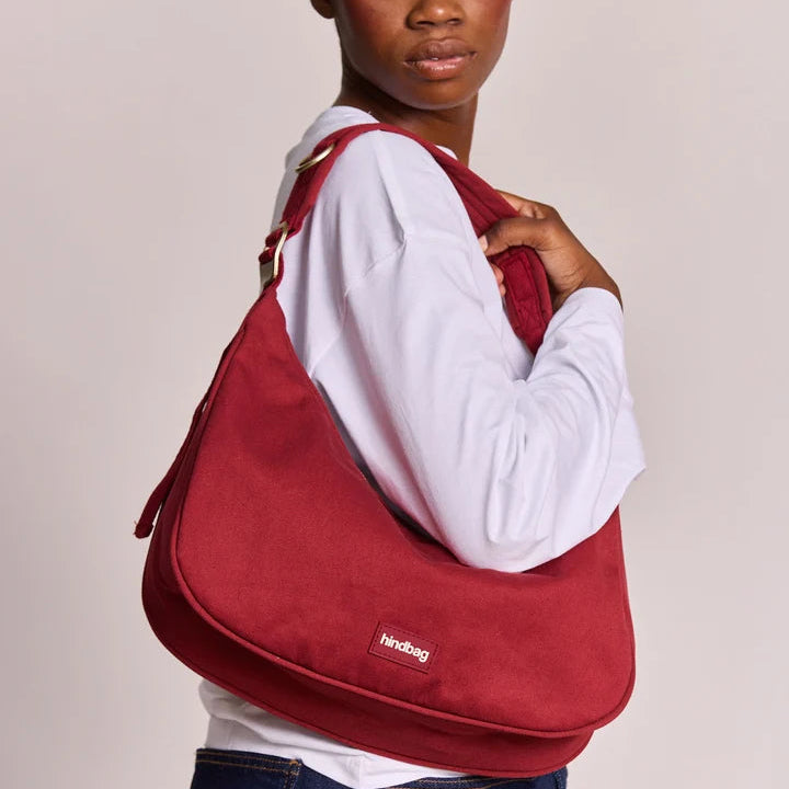 Bolso burdeos Bianca de Hindbag llevado en el hombro por una modelo con camisa blanca, mostrando su forma de hobo y la etiqueta de la marca.