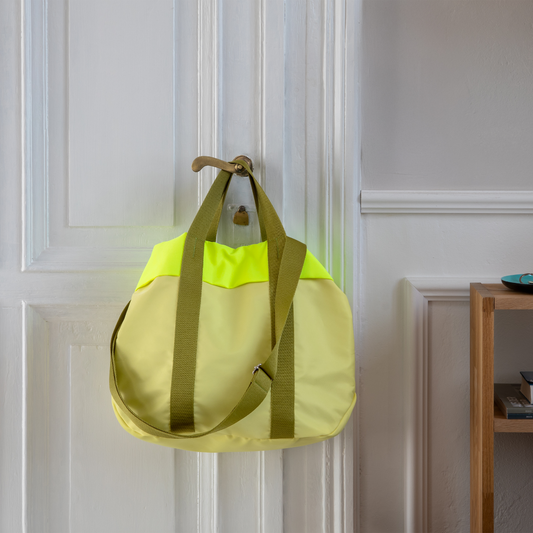 bolsa modelo nelly en color lima, con las asas de color verde oscuro, colgada del pomo de una puerta