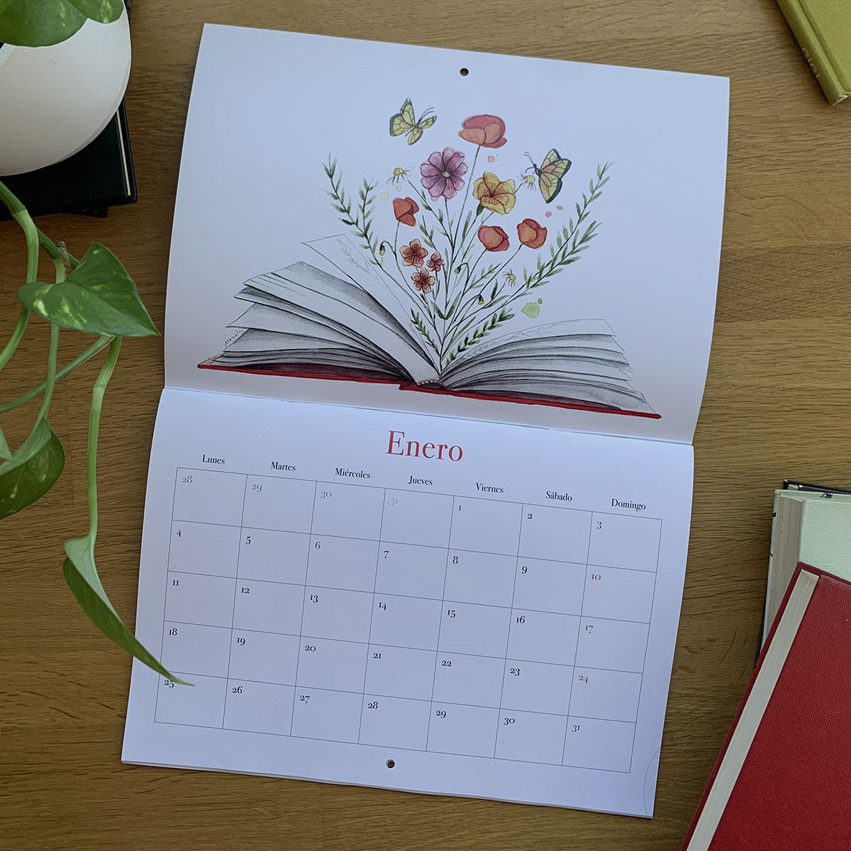 Enero del calendario 2027 Leyendo, con un libro abierto del que brotan flores y mariposas y una cuadrícula para anotaciones.
