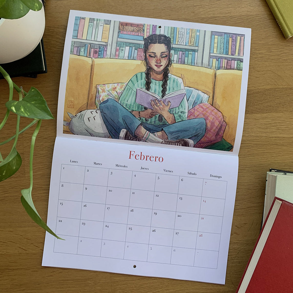 Febrero del calendario 2027 Leyendo, con una joven leyendo en un sofá amarillo delante de una estantería de libros.
