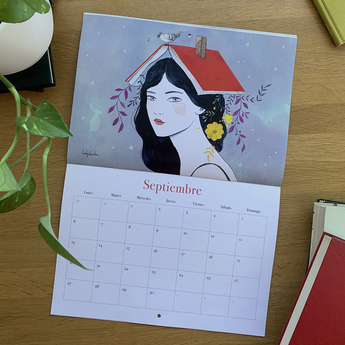 Septiembre del calendario 2027 Leyendo, con una mujer que lleva un libro abierto a modo de tejado sobre la cabeza.

