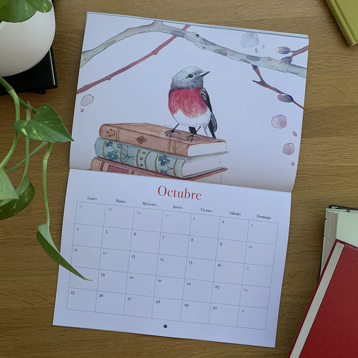 Octubre del calendario 2027 Leyendo, con un pájaro de pecho rojo sobre una pila de libros bajo unas ramas.

