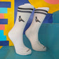 calcetines de la marca socks and co de color blanco con unas palomas en los laterales y dos bandas de color gris y negro en la parte superior sobre un fondo colorido