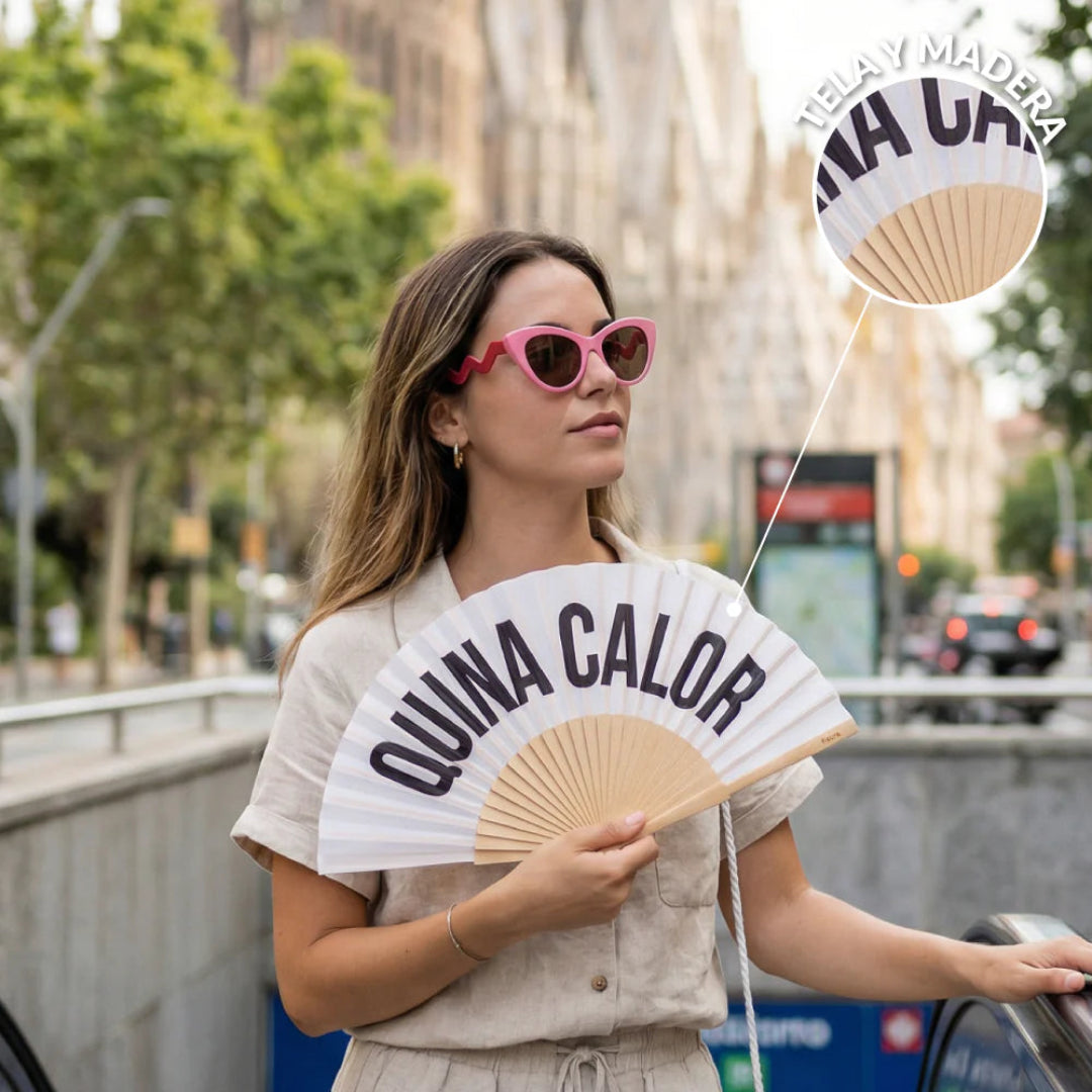 modelo con gafas de sol rosas better late than ugly y el abanico de fisura en color blanco de tela y madera con el texto en negro "QUINA CALOR" abierto 