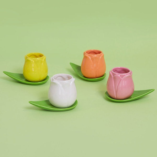 Set de tazas de café con forma de tulipanes de colores y platitos con forma de hojas sobre fondo verde