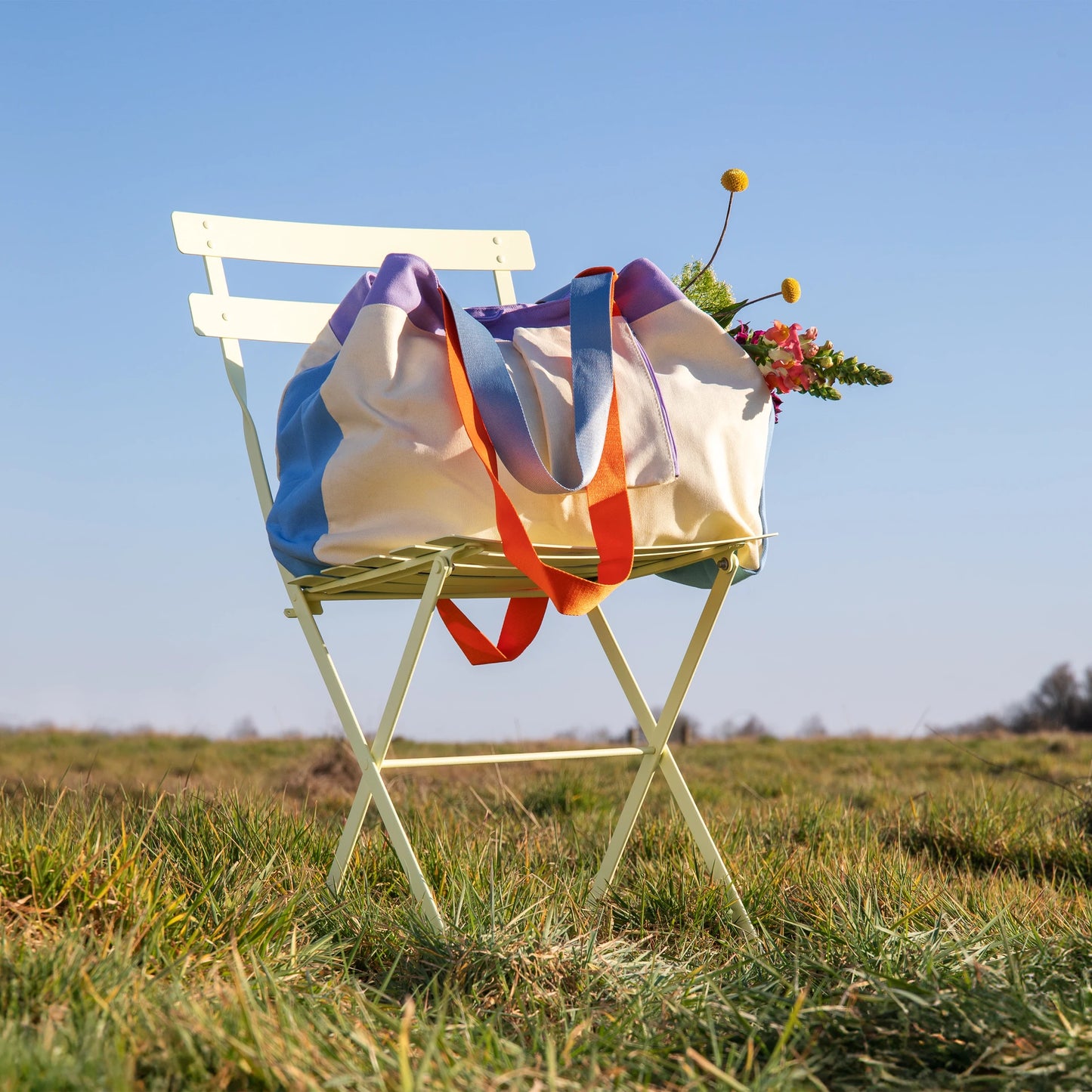 bolsa toni de la marca remember en color beige posada sobre una silla con flores dentro y en el césped