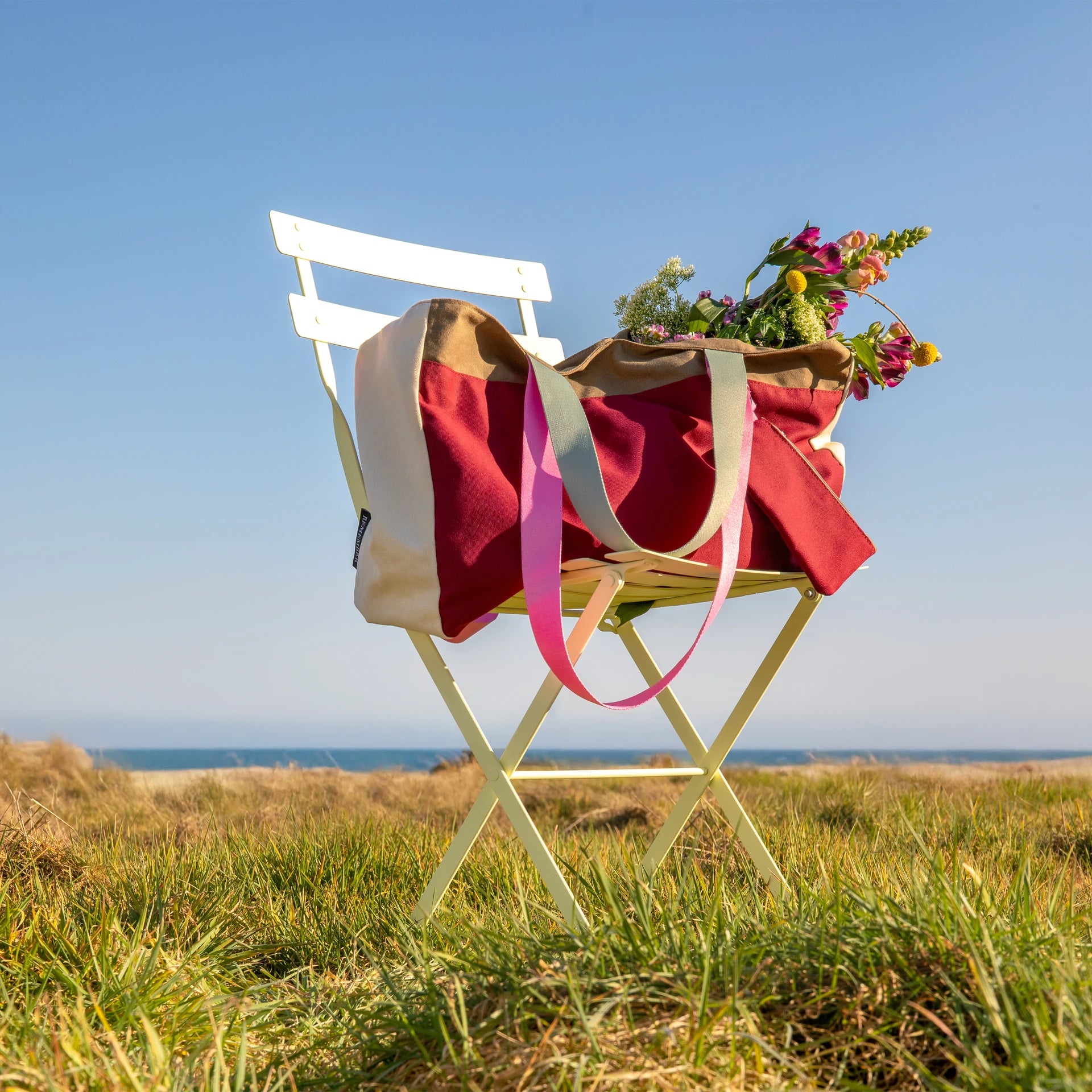 bolsa de la marca Remember en color granate sobre una silla con flores dentro y puesta en medio del campo