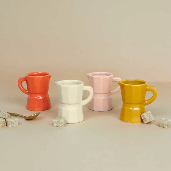 Juego de cuatro tazas de café expreso solo de cerámica de diferentes colores: naranja, blanco, caramel y rosa palo, junto a unos terrones de azúcar y una cucharilla de café