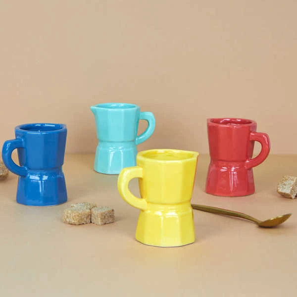 Juego de cuatro tazas de café expreso solo de cerámica de diferentes colores: azul, rosa, amarillo y turquesa junto a terrones de azúcar moreno y una cucharilla de café