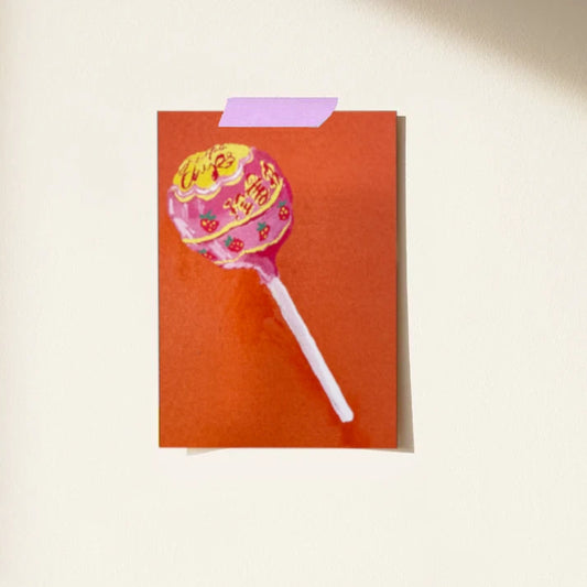 Postal con fondo rojo y un Chupa Chups de fresa sobre una pared de la artista Laura Ortíz