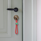 llavero colgante de cuerda roja para el móvil o las llaves con anilla plateada y un enganche con círculos de colores con una llave metida en la cerradura de una puerta 