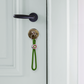 llavero colgante de cuerda verde oscuro para el móvil o las llaves con anilla plateada y un enganche con círculos de colores con una llave puesta en una cerradura de una puerta