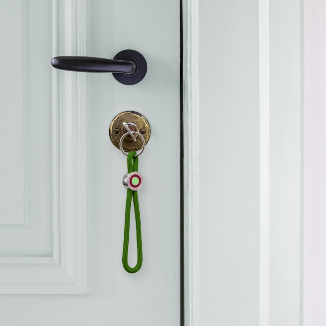 llavero colgante de cuerda verde oscuro para el móvil o las llaves con anilla plateada y un enganche con círculos de colores con una llave puesta en una cerradura de una puerta