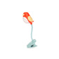 Luz de lectura roja en forma de pájaro enganchado a un libro sobre fondo blanco. 