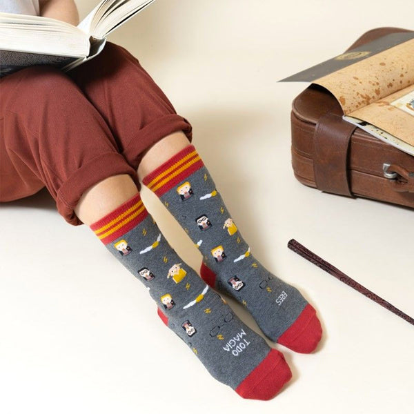 Persona leyendo con los calcetines de Harry Potter junto a una maleta y una varita mágica