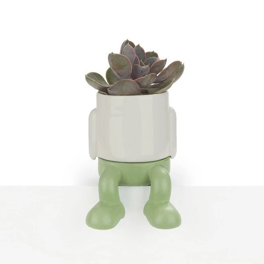 maceta mini de cerámica de color blanco con patitas colgantes de color verde, con un cactus carnoso dentro