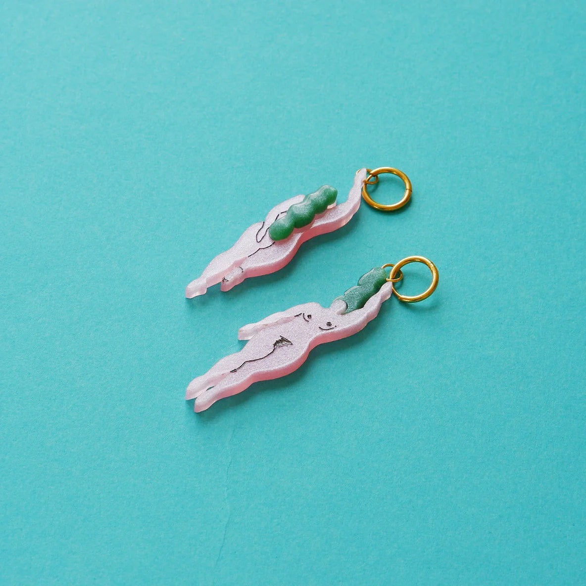 pendientes de metacrilato con aro dorado de la artista mitumi con dos mujeres nadando desnudas en color rosa con el pelo verde, sobre fondo azul