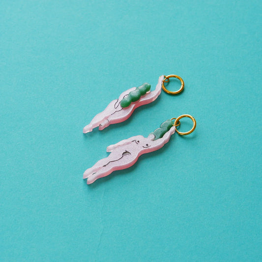 pendientes de metacrilato con aro dorado de la artista mitumi con dos mujeres nadando desnudas en color rosa con el pelo verde, sobre fondo azul