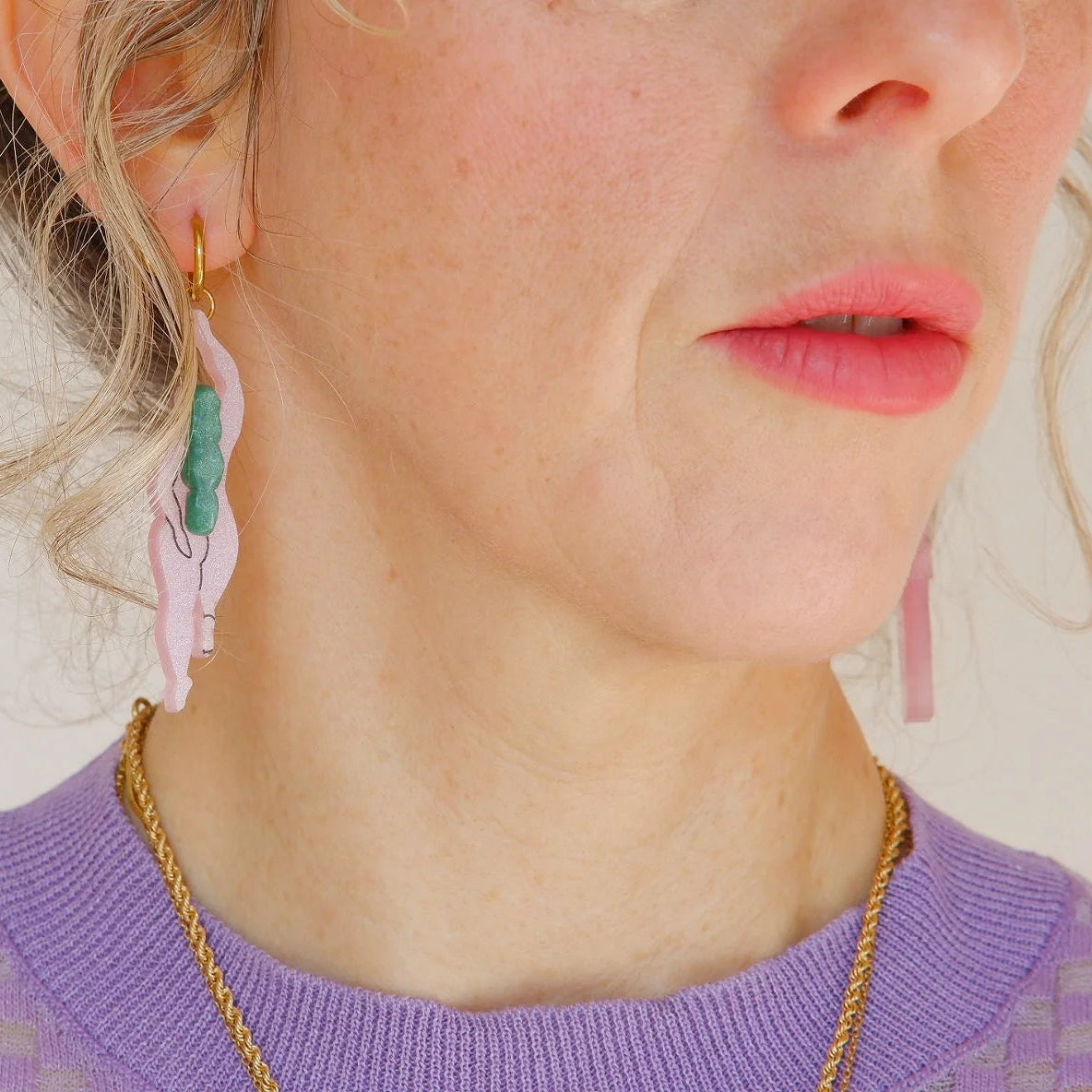 mujer llevando los pendientes de metacrilato con aro dorado de la artista mitumi con dos mujeres nadando desnudas en color rosa con el pelo verde