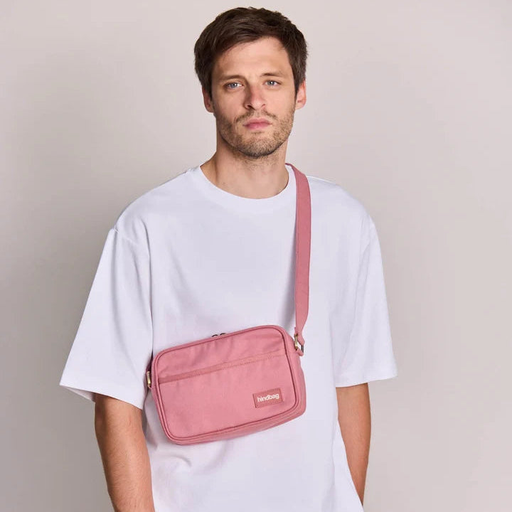 Modelo masculino con camiseta blanca y bandolera rosa Nino de Hindbag cruzada sobre el pecho.