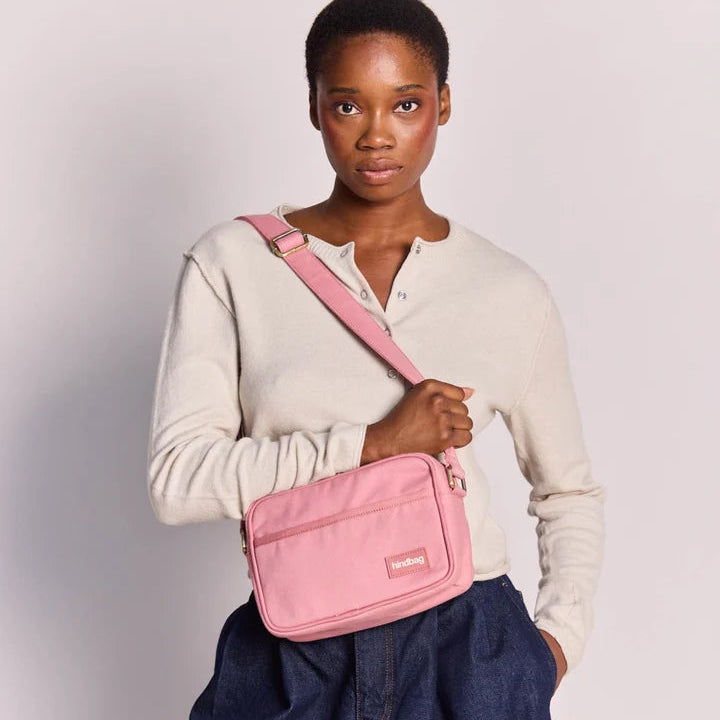 Modelo con la bandolera rosa Nino de Hindbag cruzada sobre el cuerpo, con bolsillo frontal y correa ajustable.