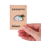 Pin divertido con diseño de dumpling kawaii de Noodoll agarrado con unos palillos verdes, cogido con una mano humana